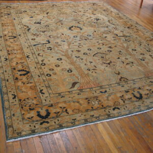 Muted rug with tan and light green Tree of Life pattern sits on wide plank hardwood flooring.