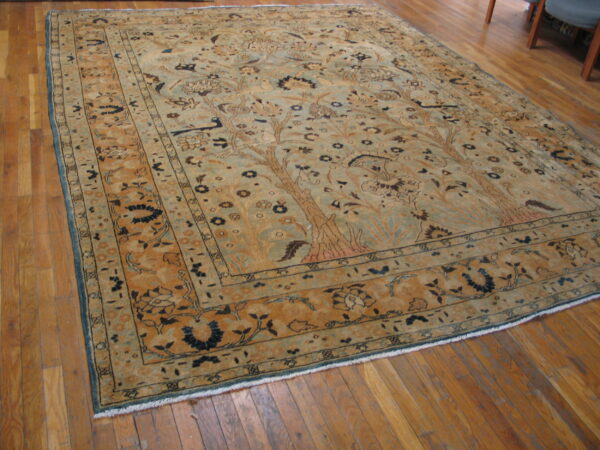 Muted rug with tan and light green tree of life pattern sits on wide plank hardwood flooring.