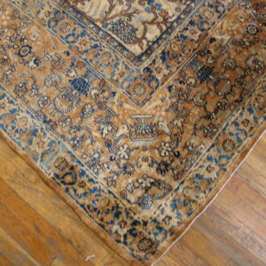 Ornate gold and dark blue floral rug border detail rests on worn, light brown wood flooring.