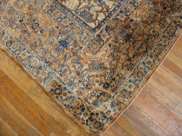Ornate gold and dark blue floral rug border detail rests on worn, light brown wood flooring.