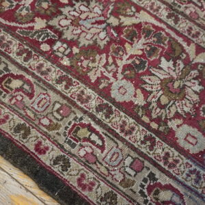 Low-pile patterned rug in deep red, tan, and faded gray rests on old, distressed wood planks.