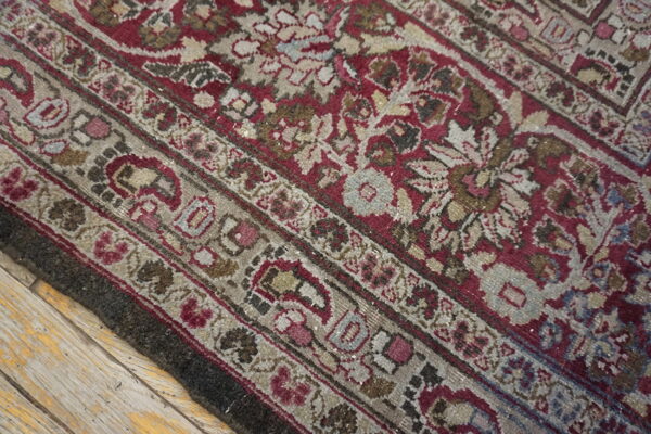 Low-pile patterned rug in deep red, tan, and faded gray rests on old, distressed wood planks.