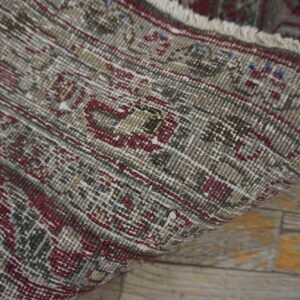 Distressed gray and burgundy patterned rug detail showing the edge and fringe on light wood flooring.