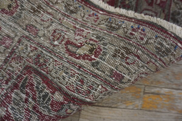 Distressed gray and burgundy patterned rug detail showing the edge and fringe on light wood flooring.
