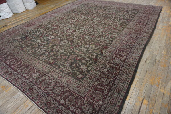 Low-pile rug with dark floral pattern in maroon and sage rests on light wood floors near white storage bags.