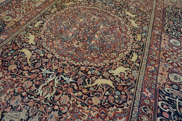 Ornate traditional rug with a deep navy field, red medallion, and repeating beige animal motifs.