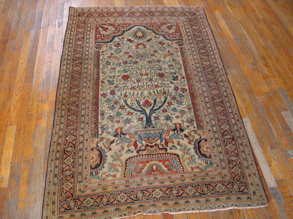 Low-pile beige, blue, and red traditional rug displaying a tree of life design on hardwood floors.