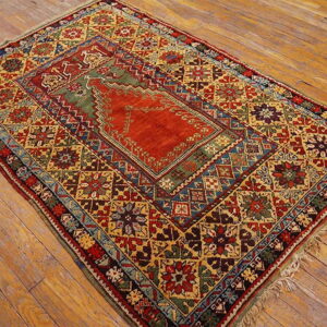 Low-pile rug with rust and olive geometric patterns and intricate borders rests on light brown wood flooring.