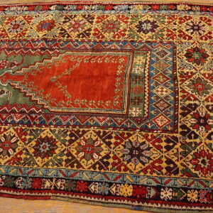 Geometric low-pile rug in red, yellow, green, and blue, featuring a central medallion, resting on wood floor.