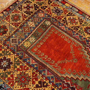 Highly detailed rug with a dense geometric pattern in red, gold, blue, and green on a wood floor.