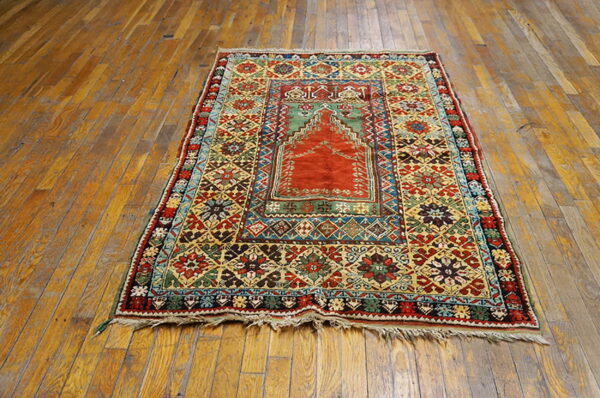 Ornate, multi-color rug with a central red arched design rests on weathered wood floors.