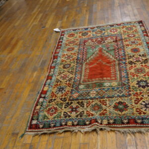 A small red, gold, and blue patterned rug with fringe rests on distressed hardwood flooring.