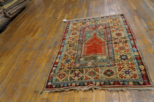A small red, gold, and blue patterned rug with fringe rests on distressed hardwood flooring.