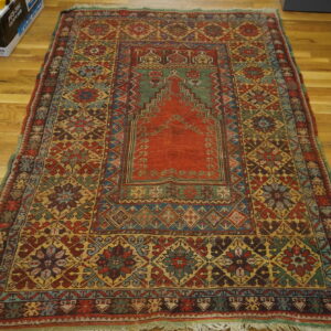 Multicolored rug with a central stepped red and green design placed on a honey-toned wood floor.