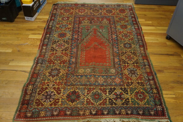 Multicolored rug with a central stepped red and green design placed on a honey-toned wood floor.