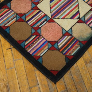 Multicolored geometric hooked rug featuring striped and solid patches resting on rustic wood flooring.