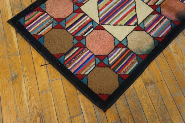 Multicolored geometric hooked rug featuring striped and solid patches resting on rustic wood flooring.