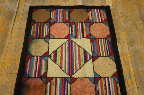 Patchwork rug with multicolored stripes, beige, and brown octagons, framed by a black border on worn yellow wooden flooring.
