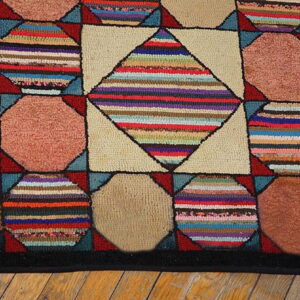 Hooked rug with multicolored striped diamonds and solid brown/rose octagons on light wood flooring.