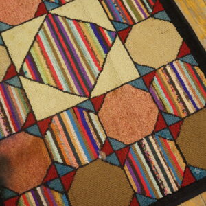 Patchwork rug with beige octagons and multicolored striped diamonds bordered by black on wooden planks.