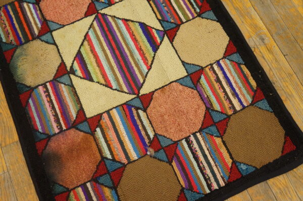 Patchwork rug with beige octagons and multicolored striped diamonds bordered by black on wooden planks.