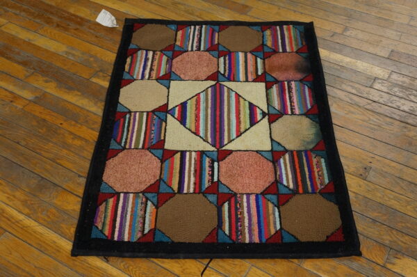 Geometric hooked rug featuring multicolored stripes and solid shapes, bordered in black on wood floors.