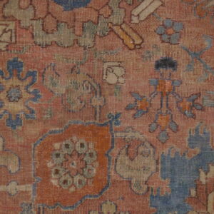 Muted red-orange rug detail showing low pile and traditional patterns in blue, yellow, and brown.