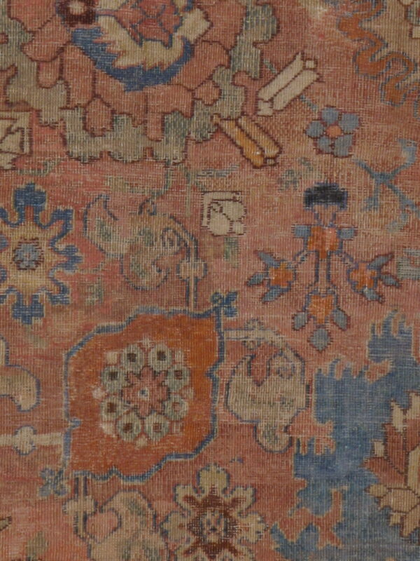 Muted red-orange rug detail showing low pile and traditional patterns in blue, yellow, and brown.