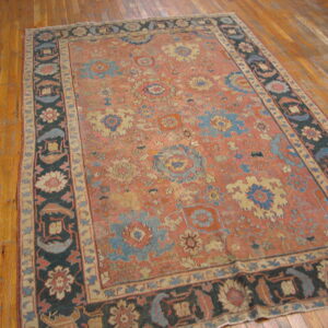 Distressed coral rug featuring scattered blue and cream floral motifs, bordered in dark navy on wood planks.