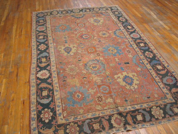 Distressed coral rug featuring scattered blue and cream floral motifs, bordered in dark navy on wood planks.