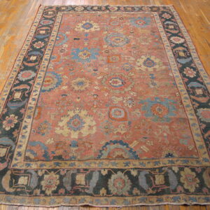 Distressed rug featuring a salmon field, detailed blue and cream medallions, and a wide dark border on wood.