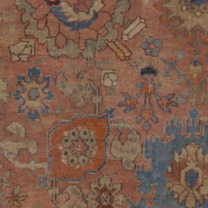 Close-up of a distressed traditional rug with a terracotta field and ornate motifs in blue, tan, and orange.