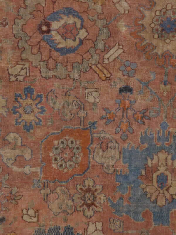 Close-up of a distressed traditional rug with a terracotta field and ornate motifs in blue, tan, and orange.