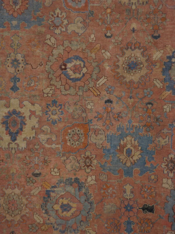 Intricate, low-pile rug pattern featuring faded traditional floral motifs in blue, rose, and beige.