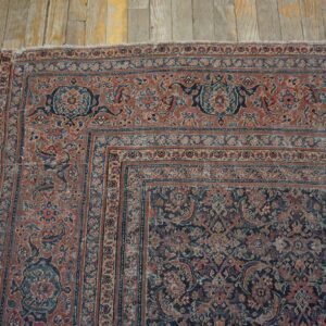 Low-pile, traditional rug in faded rust and navy botanical patterns rests on worn wooden planks.