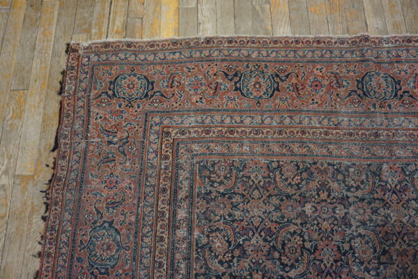 Low-pile, traditional rug in faded rust and navy botanical patterns rests on worn wooden planks.