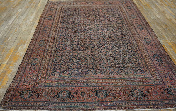 Traditional rug with dense floral navy and rust pattern resting on rustic wooden planks.