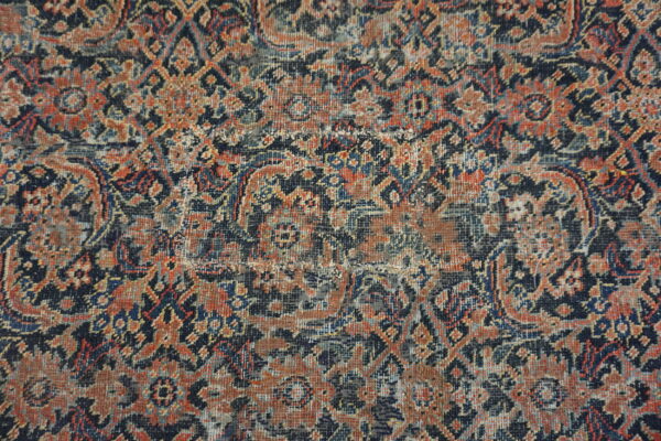 Intricate traditional rug pattern featuring colors of navy, burnt orange, and gray with a worn, low pile.