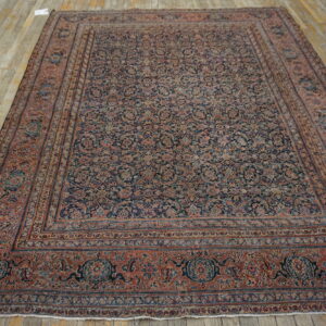 Large low-pile rug featuring an intricate all-over floral pattern in muted red and dark navy on wood planks.