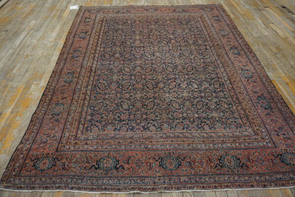 Large low-pile rug featuring an intricate all-over floral pattern in muted red and dark navy on wood planks.