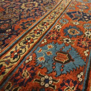 Navy, rust, and turquoise floral rug detail shows multiple patterned borders and soft texture on wood flooring.