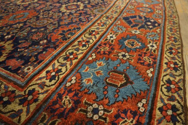 Navy, rust, and turquoise floral rug detail shows multiple patterned borders and soft texture on wood flooring.