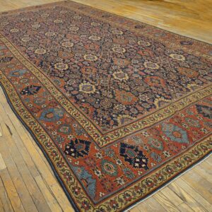 Ornate area rug in navy, terracotta, and gold with a low pile, placed on light plank wood flooring.