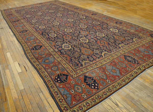 Ornate area rug in navy, terracotta, and gold with a low pile, placed on light plank wood flooring.