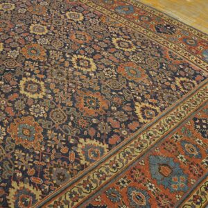 Navy rug featuring a dense, traditional floral pattern in rust, blue, and gold on pale wood flooring.