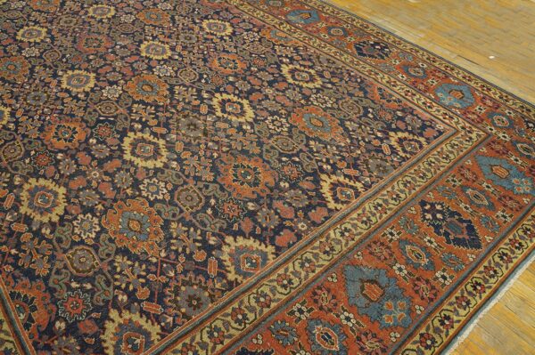 Navy rug featuring a dense, traditional floral pattern in rust, blue, and gold on pale wood flooring.