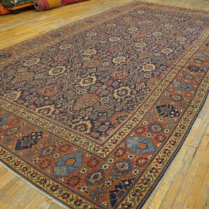 Traditional navy and rust rug with dense floral designs displayed on distressed wood floors.