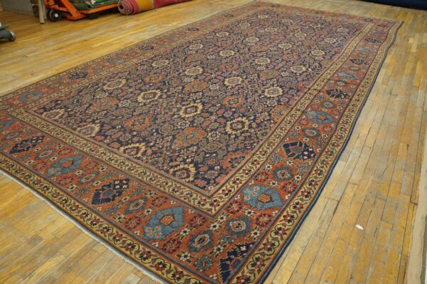 Traditional navy and rust rug with dense floral designs displayed on distressed wood floors.