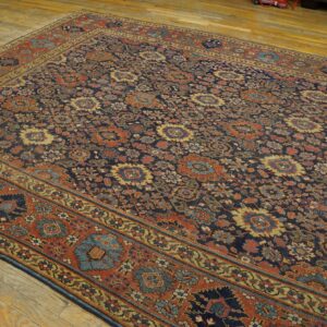 A low-pile rug featuring a dense floral pattern in dark blue, terracotta, and gold on wood flooring.