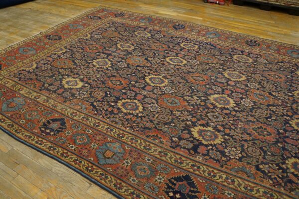 A low-pile rug featuring a dense floral pattern in dark blue, terracotta, and gold on wood flooring.